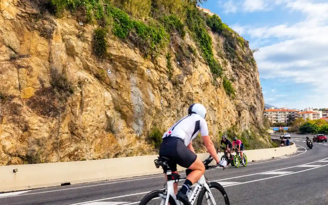 Ciclista en carretera costera durante IRONMAN Barcelona con faro de Calella de fondo